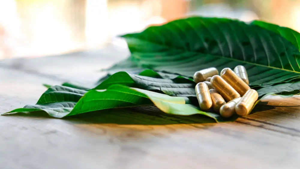 Foglie di kratom su un tavolo con capsule di kratom